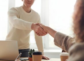 Close-up of professionals shaking hands over coffee in a modern office.